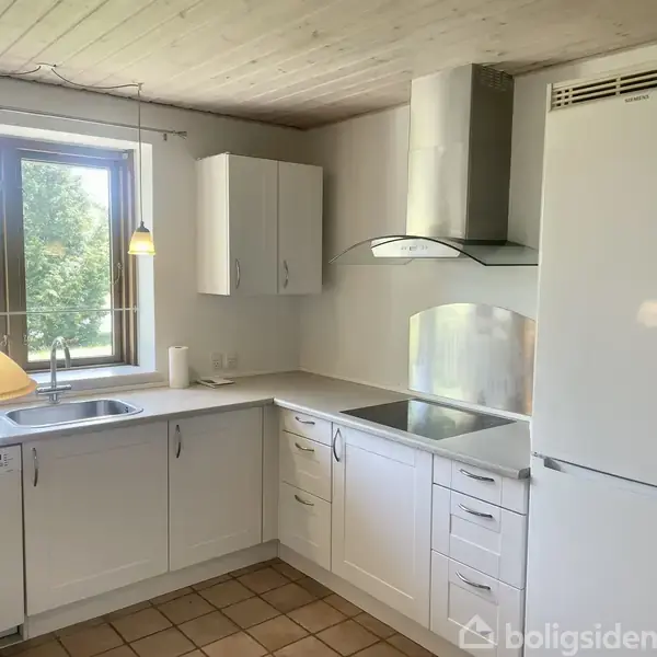 Et rum med to polstrede stole ved et lille bord; en firkantet lampe hænger over et spisebord. En dør åbner til et tilstødende værelse. Store vinduer viser en have.