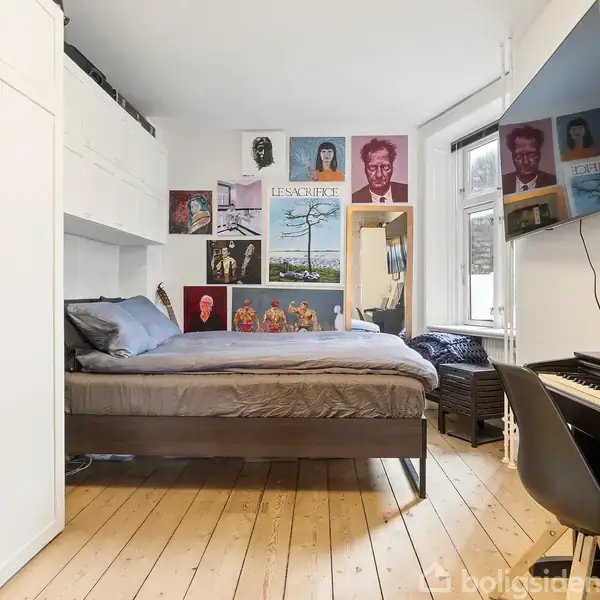 Et soveværelse med en seng i midten, omgivet af plakater på væggen. Til højre ses et tv monteret på væggen, og en digital klaver står ved siden af i rummets hjørne.