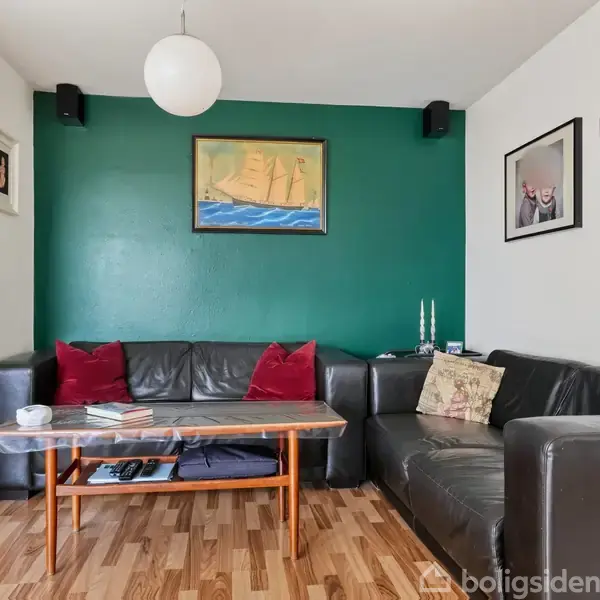 Sort læderhjørnesofa står op ad en væg i en stue med trægulv. Et mørkegrønt maleri hænger over sofaen. Et lille bord med bøger og lysestager står foran sofaen.
