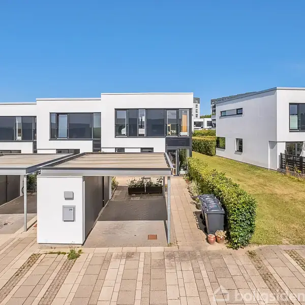 Rækkehuse i moderne stil, stillet i en række, med carporte i forgrunden og velplejede græsplæner på hver side. Klar blå himmel i baggrunden.