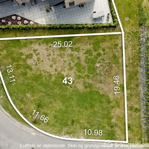 Græsplæne markeret med hvide linjer og tal, herunder 25.02, 19.46, 10.98, 17.66, 13.11, og tallet 43 i midten. Omgivet af indkørsler og bygning. Tekst: "Luftfoto er vejledende. Skel og grundgrænser er ikke nødvendigvis korrekt vist."