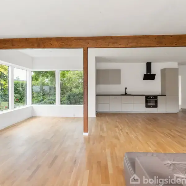 Et moderne badeværelse med en væghængt toilet, glasafskærmet bruser til venstre og en vask på et træskab til højre. Væggene er beige, og gulvet er lyst.