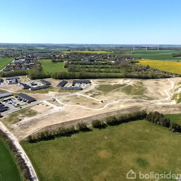 Byområde under udvikling med nybyggede huse spredt rundt på en delvist gravet grund, omgivet af grønne marker og skove. Boligsiden-logo ses nederst i billedet.