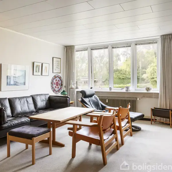 En stue med en sort lædersofa og træstole omkring et træbord. Store vinduer lader lys ind, mens bogreoler og malerier dekorerer rummet.