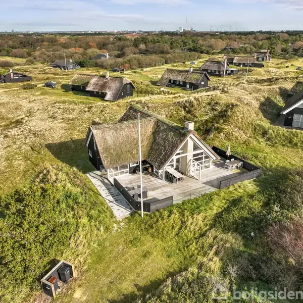 Stråtækt hus står stille på en bakketop, omgivet af græs på en åben naturgrund. Flere lignende huse ses i baggrunden, spredt i et kuperet landskab.