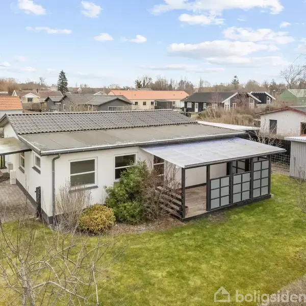 Huset står stille, omgivet af en velholdt have med buske og et græsområde. Det har et tag af metal og en overdækket terrasse, beliggende i et roligt nabolag.