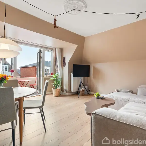 Stue med hvid sofa, sofabord og TV, åbner ud til altan med rødt bord. Spisebord ved siden af, dekoreret med blomster. Lyse trægulve og beige vægge.