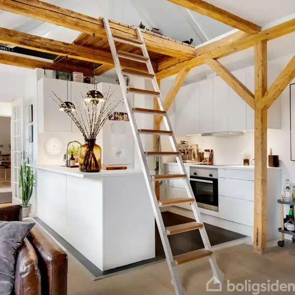 TV hænger på en rå murstensvæg, omgivet af moderne møbler i en stue med en skrå loft. En hylde fyldt med bøger står i hjørnet nær en døråbning.