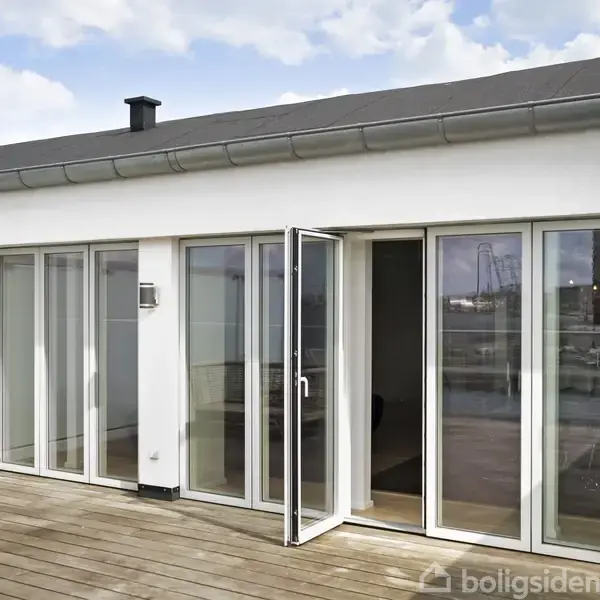 Terrasse med glasdøre åbner op til et moderne hjem. Trægulvet omkranser området, mens skyer og himmel ses ovenfor. Boligsiden watermark ses nederst i højre hjørne.