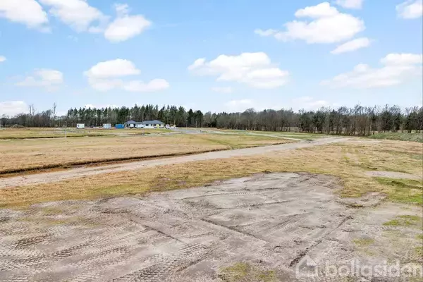 Niveau markeret jord med spor af dæk; handlede som byggeplads i et åbent, græsarealområde med et hus og skov i baggrunden under en blå himmel med skyer.