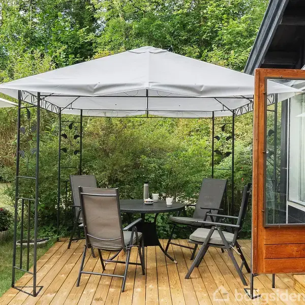 Pavillon med fire stole og et bord står på en træterrasse. Omkring er der grøn bevoksning, og terrassedøren står åben ind til huset.