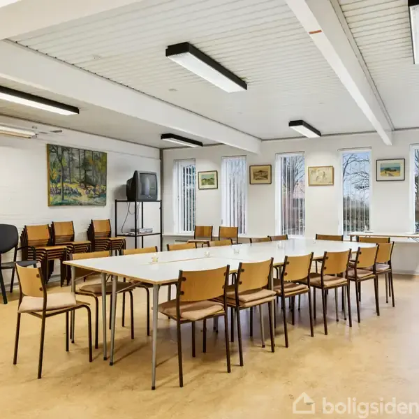 Et mødelokale med stole omkring to lange borde. Tv'et står på stativ i hjørnet. Kunstværker hænger på væggene. Rummet har store vinduer og lys loftbelysning.