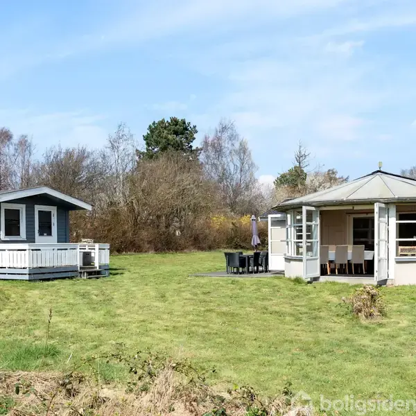 To huse står på en græsplæne. Det ene hus er lille og blåt med en veranda, mens det andet er lyst og ottekantet med store vinduer.