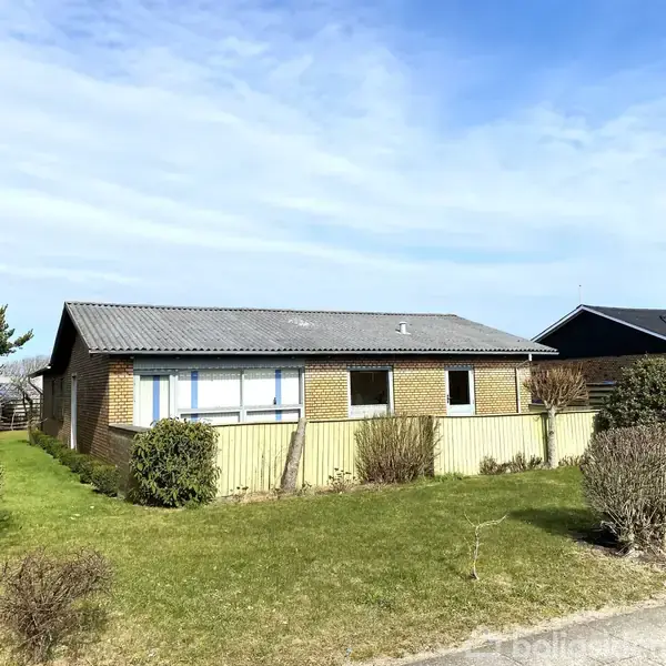 Et enfamiliehus af mursten står stille i en forstadshave med grønne buske og græsplæne. Skyfri blå himmel ses i baggrunden.