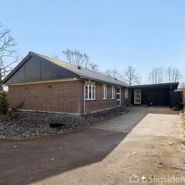 En murstensvilla står i et kuperet, brolagt indkørselsområde omgivet af bartræer. Huset har et skråt tag og ligger i en åben, skovrig beliggenhed med stille vinterskov i baggrunden.