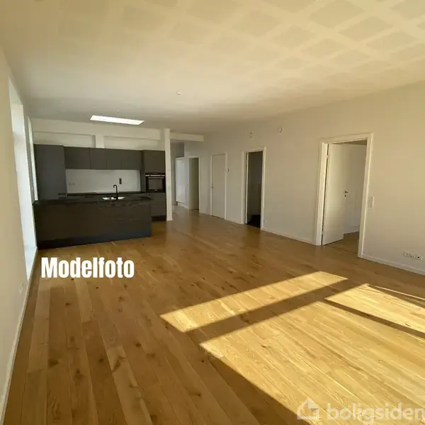 Køkken i moderne lejlighed, uden møbler, med trægulv og grå skabe, i et lyst rum. Tekst: "Modelfoto".