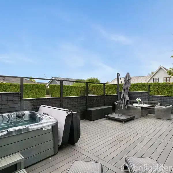 Boblebad står ubenyttet på en moderne terrasse med trædæk og udendørsmøbler. Omkring er høje hegn og hække, der giver privatliv i et fredeligt boligområde.