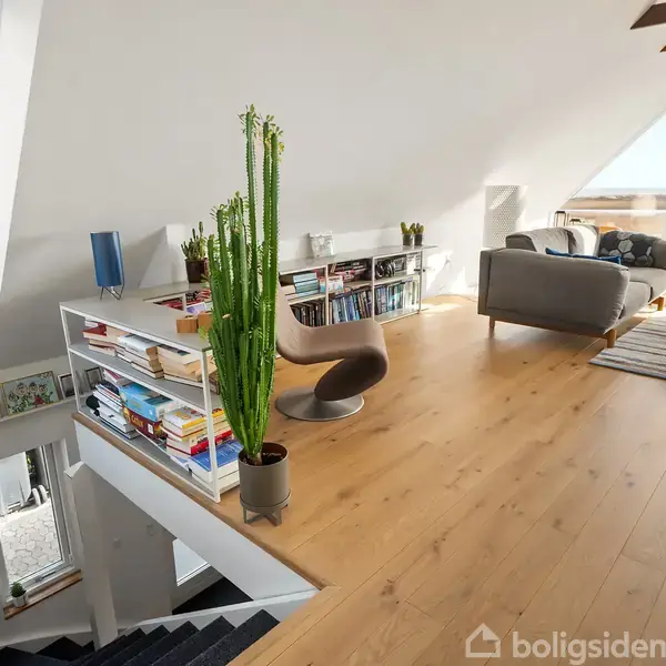Et moderne loftsrum har en stor bogreol fyldt med bøger og planter, hvor en stol står foran. Det store vindue afslører natur udenfor, og en sofa står i nærheden.