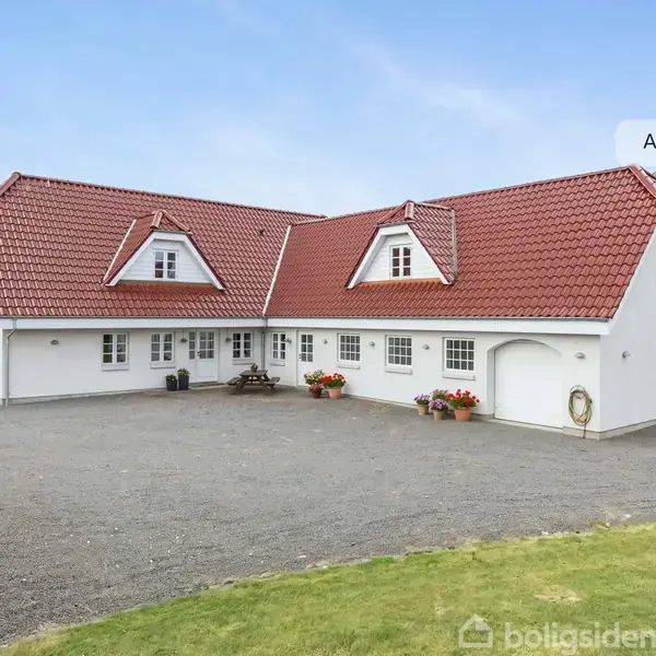 Hus med rødt tegltag, hvide vægge og flere kviste. Foran huset er en grusbelagt gårdsplads med blomsterkrukker. Til venstre ses græs og buske. Tekst: "AI visualisering".