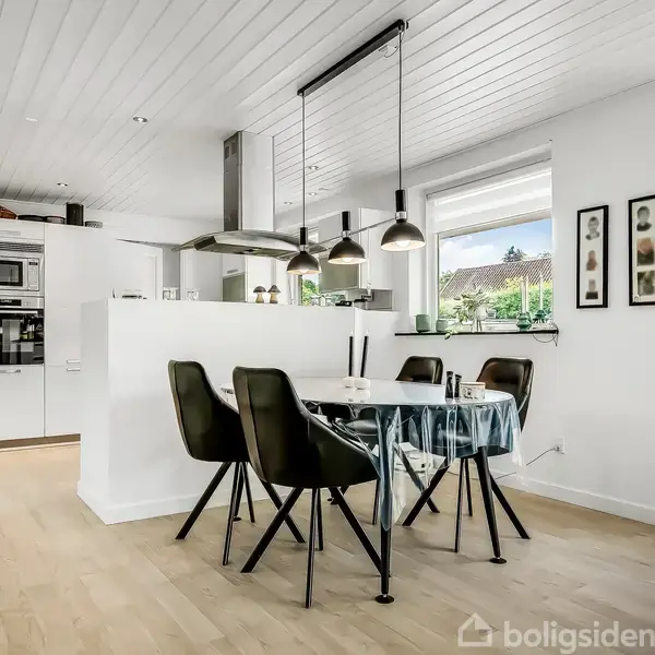 Rækkehus og carport med en hvid bil parkeret, placeret ved en grusplads. Rækkehuset er i røde mursten. Adressen "58" vises ved entrédøren, omgivet af grønne planter og blå himmel.