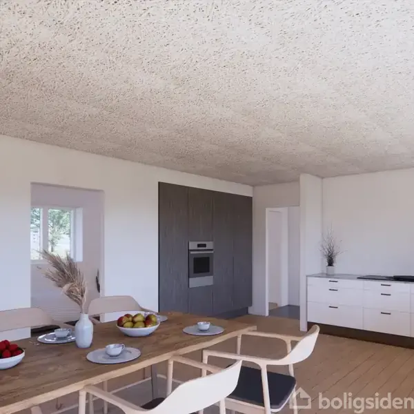 Et moderne køkken med et træbord dækket med tallerkener og skåle. I baggrunden ses hvide skabe, en indbygget ovn og dekorative vaser. Rummet er lyst og rummeligt.