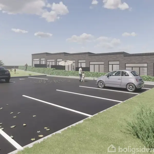Bygning med fladt tag omgivet af grønne plæner. Flere biler parkeret på en vej ved siden af. Skyer ses på en blå himmel, og en person går på parkeringspladsen.