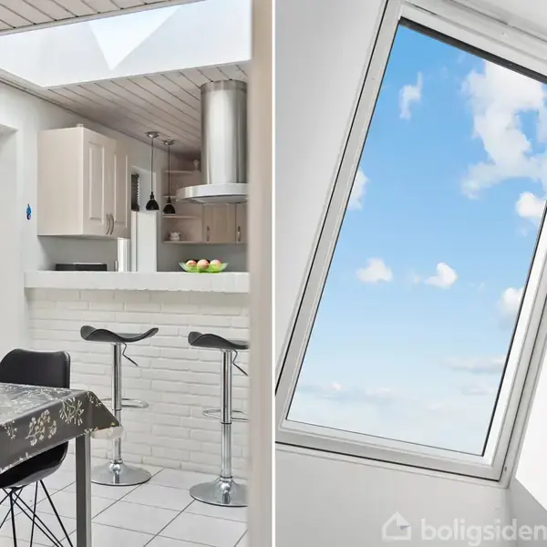 Moderne køkken-alrum med spisebord dækket med dug, stole og barstole ved køkkenø. Loftsvindue slipper lys ind. Ved siden ses et skråvindue med udsigt til en blå, skyet himmel.