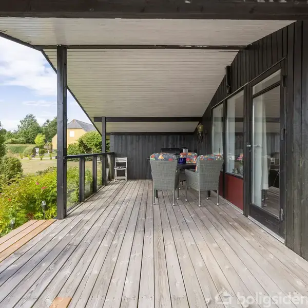 Træterrasse med borde og stole, under overdækning, i forstadsområde med have.