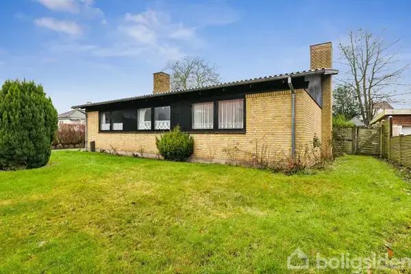 Et en-familiehus af mursten står stille på en velplejet græsplæne med en blå himmel i baggrunden. To skorstene ses på taget.