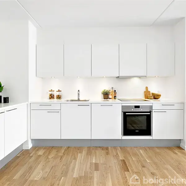 Lyst, moderne køkken med hvide skabe, integreret ovn og håndvask. Trægulv og dekorative elementer som planter og opbevaringskrukker skaber en indbydende atmosfære. Vandtæt, minimalistisk design.