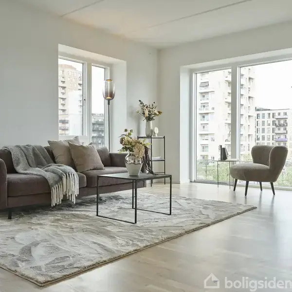En moderne stue indeholder en brun sofa med tæppe, placeret ved et sofabord med blomsterdekoration. Store vinduer viser udsigt til byens bygninger, suppleret af grønne planter.