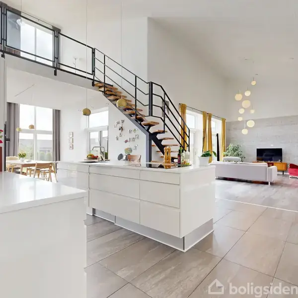Hvidt køkken med ø, trappe op til repos, i et moderne åbent stueområde. Stuen har store vinduer, et hjørne med sofaer og loftslamper, hvilket skaber et lyst og luftigt miljø.