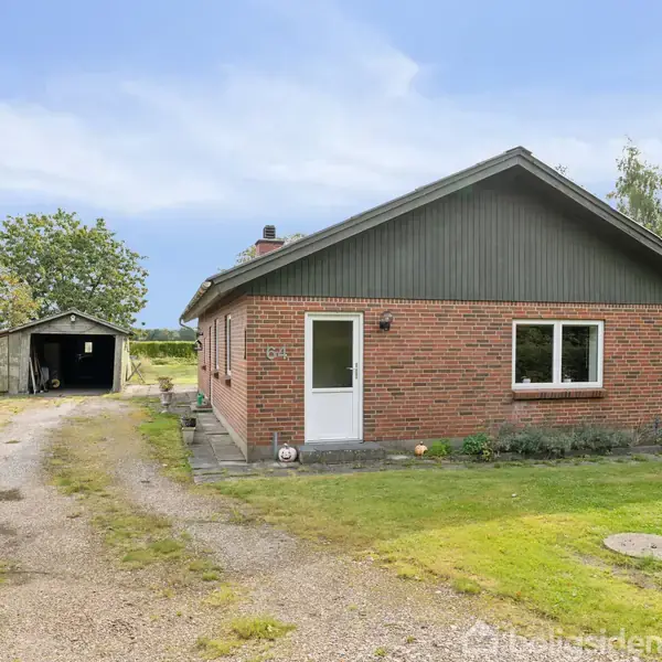 Et enkelt murstenshus står stille i en grøn have, foran en grusvej der fører til en åben garage. Skyfri blå himmel og tæt bevoksning omgiver huset.