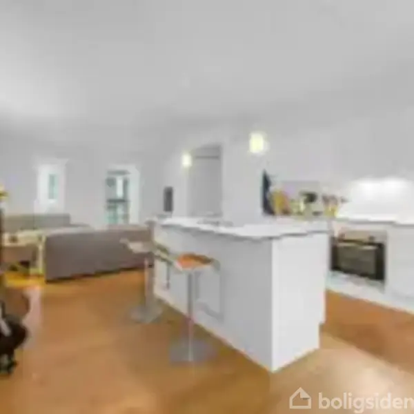 Et lyst køkken med en moderne hvid ø, to høje stole og apparater omkring. I baggrunden ses en stue med sofa og dekorationer, alt på en trægulvsoverflade.