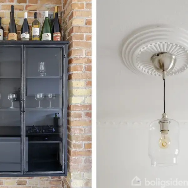 Et glasskab med vinflasker og glas står mod en murstensvæg. Ved siden af hænger en loftslampe med en glaspære fra en roset.