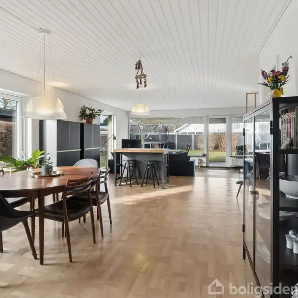 Et lille hus med skråtag står på en brolagt gårdsplads. Det har murede vægge og en garage ved siden af. Omgivet af et hegn og en græsplæne.