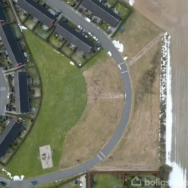 Veje og rækkehuse ses fra oven, omkransende en grøn park med en legeplads. Et grusområde grænser op til mark. Snepletter er spredt omkring. Ingen tekst til stede.