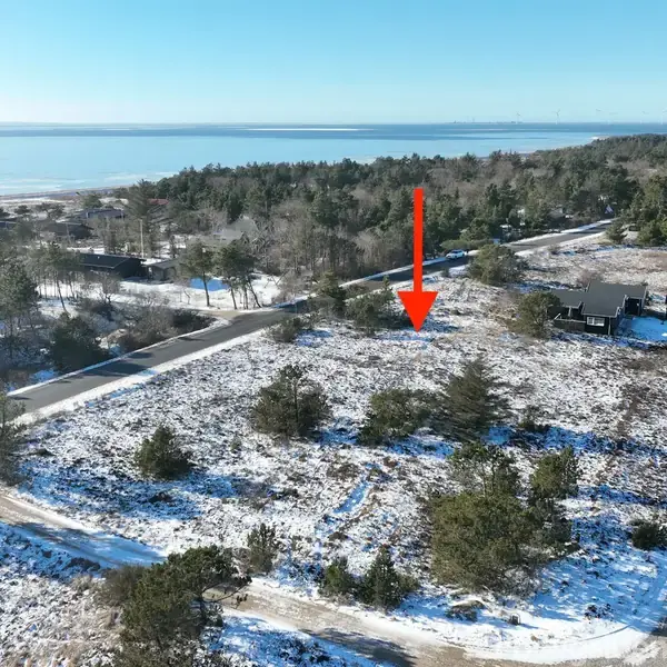 Rødt pil markerer en sneklædt grund omgivet af træer og buske. Området ligger nær kysten med en udsigt over havet. Flere veje grænser op til grunden.