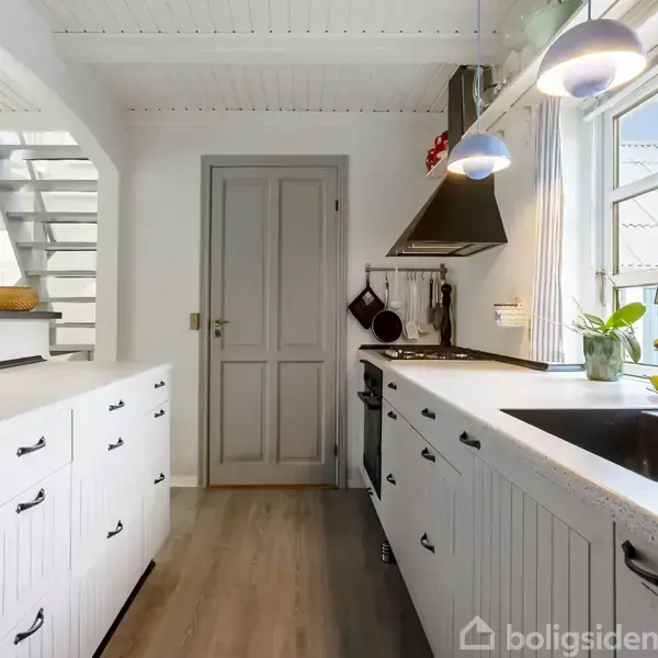 Et moderne køkken med hvide skabslåger og sort bordplade. Handlingen er stilstanden, med arrangeret frugt på bordet. I konteksten er der et vindue med udsigt til husets ydre.