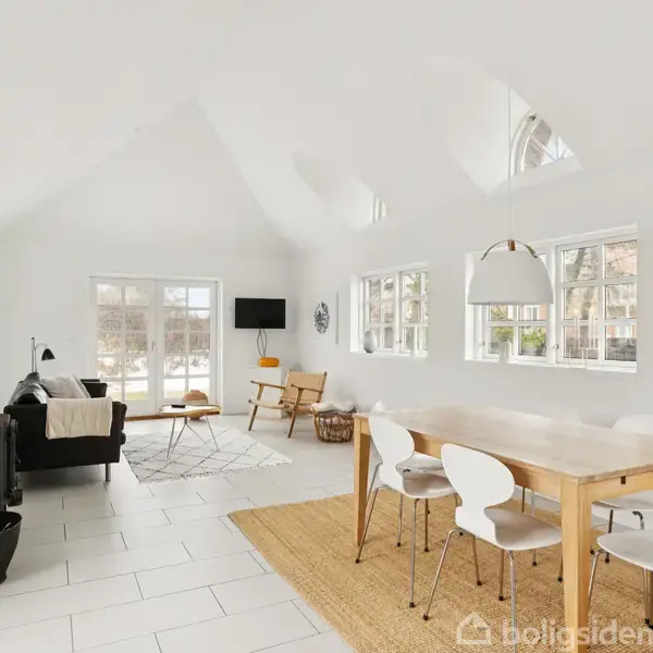 Stråtækt hus med mørk træfacade, vinduer med buede rammer; står i en grøn have med græs og vilde blomster. Nummer 11 på huset.