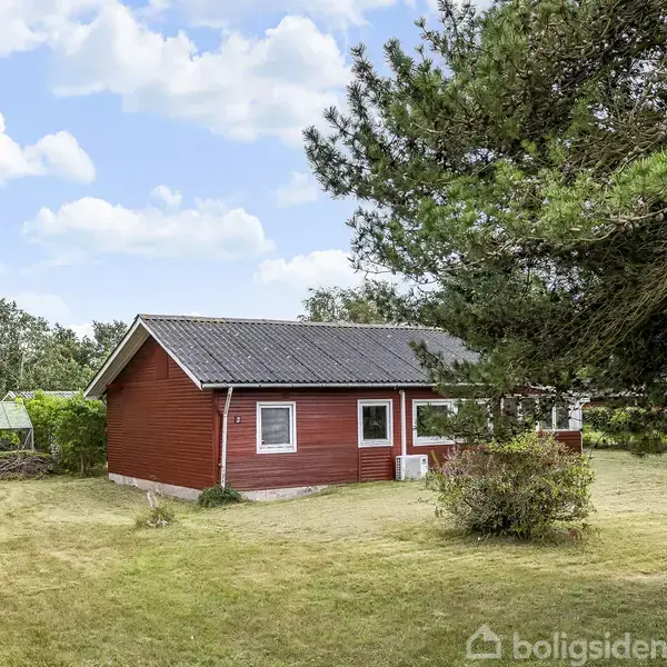 Et rødt hus står stille i en stor, grøn have med græs og træer. I baggrunden ses en blå himmel med lette skyer.