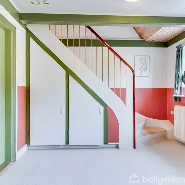 Trappe med grønne trin og rød gelænder, i et rum med grøn- og rødmalede vægge. Der står sko på gulvet ved et vindue med gardiner og en plante i vindueskarmen.