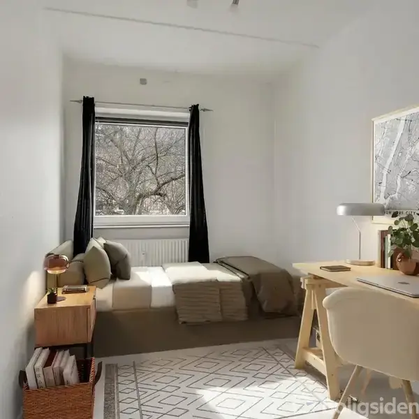 Et lyst værelse med en enkeltseng under et vindue og et skrivebord til højre. Rummet er indrettet med et tæppe, hylder og dekorationer i en minimalistisk stil.