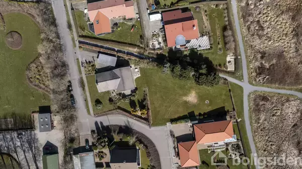 Boliger med røde tage er placeret langs snoede veje i et grønt område. Omkring husene ses haver og træer. En sti løber til højre gennem en naturlig beplantning. Text: "Boligsiden."