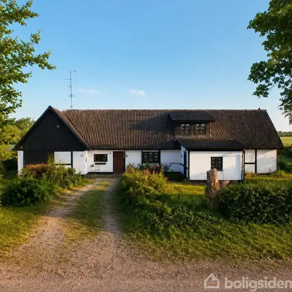 Et landligt hus står i en frodig have med grusindkørsel. Huset har hvid facade og mørkt tag. Træer og grønne buske omgiver området på en solrig dag.