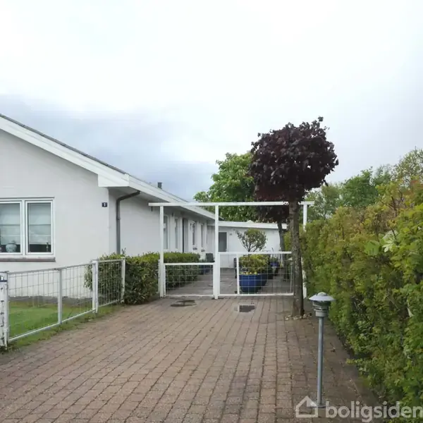 Et skrivebord med stol står foran en bogreol fyldt med bøger. Der er en dør med glasruder bagved. Tæpper ligger på en stol, og der er en farverig tæppe på gulvet.