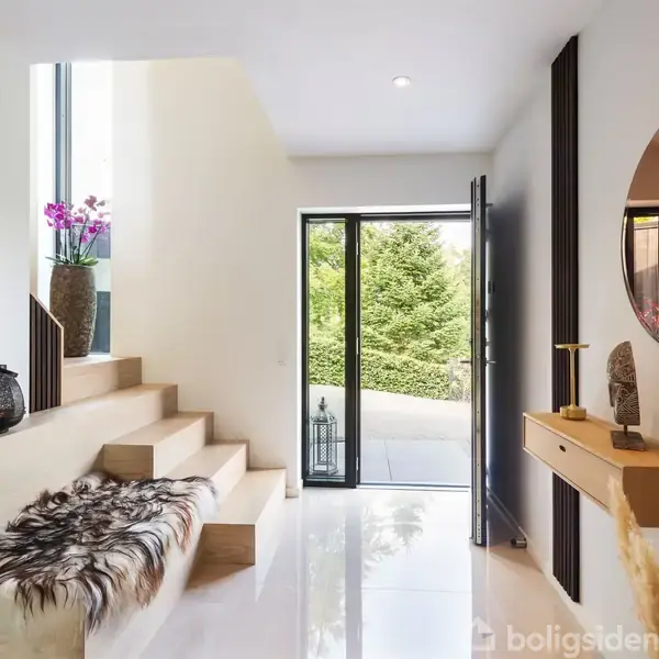 Trappe med pelstæppe fører op til vindue med plante; moderne indgang med spejl, konsolbord og åben dør ud mod have.