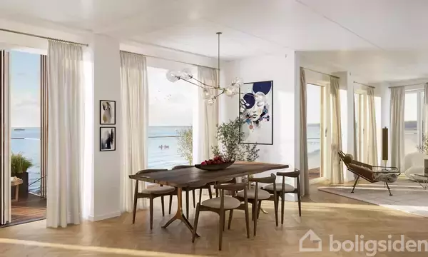 Spisebord med stole er stillet i en lys stue med store vinduer, der viser havudsigt. Et stort, moderne lysekrone hænger over bordet.