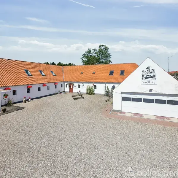 Hvid bondegård med rødt tegltag omgiver en stor grusbelagt gårdsplads. På bygningens gavl står teksten "Den Store Bondegård" under en tegning af en hest og en gris.