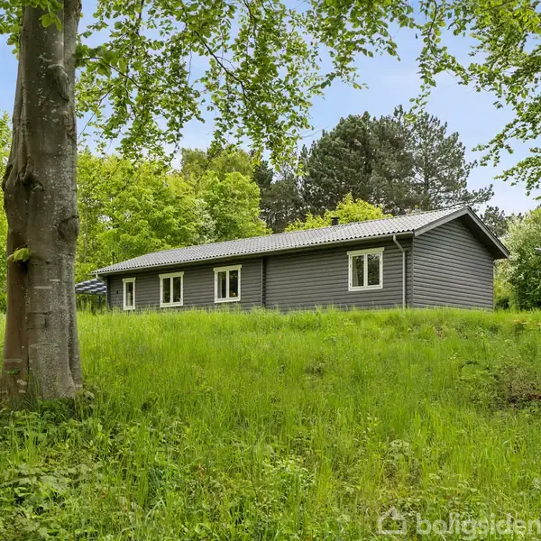 Gråt hus står stille omgivet af frodige grønne træer og græs i en skovklædt have.